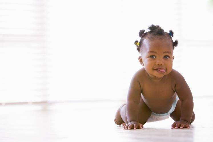 10 month old baby girl with dark skin tone and tiny pigtails crawling towards camera with tongue out