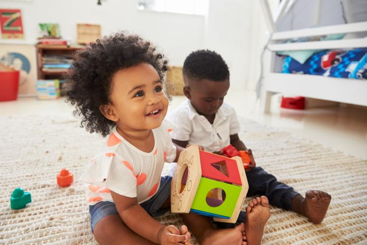 23 month olds playing on the floor with a shape sorter in bedroom.