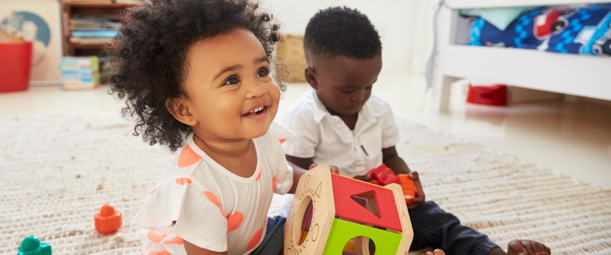 23 month olds playing on the floor with a shape sorter in bedroom.