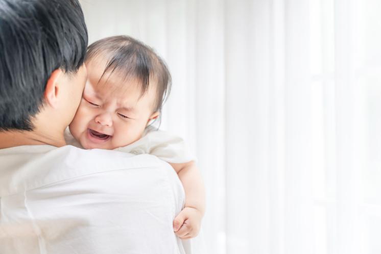 Tired 4 month old baby cries on dad's shoulder