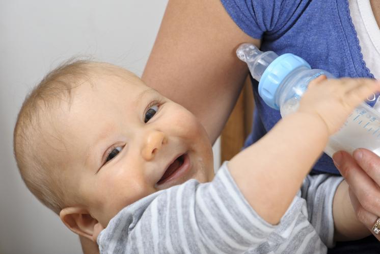 baby being held by mom and offered bottle