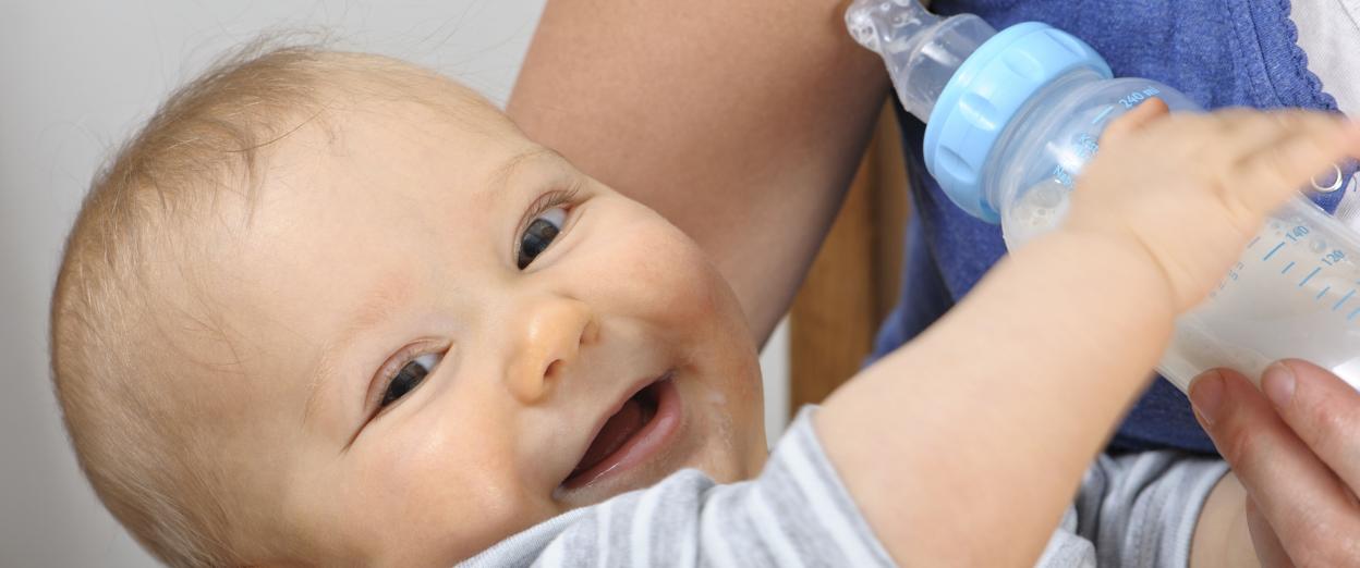 baby being held by mom and offered bottle