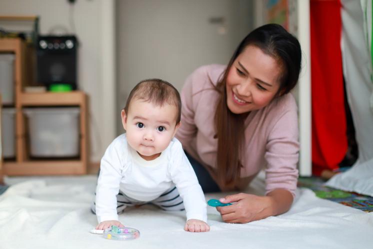 baby on hand and knees with mom behind smiling at baby
