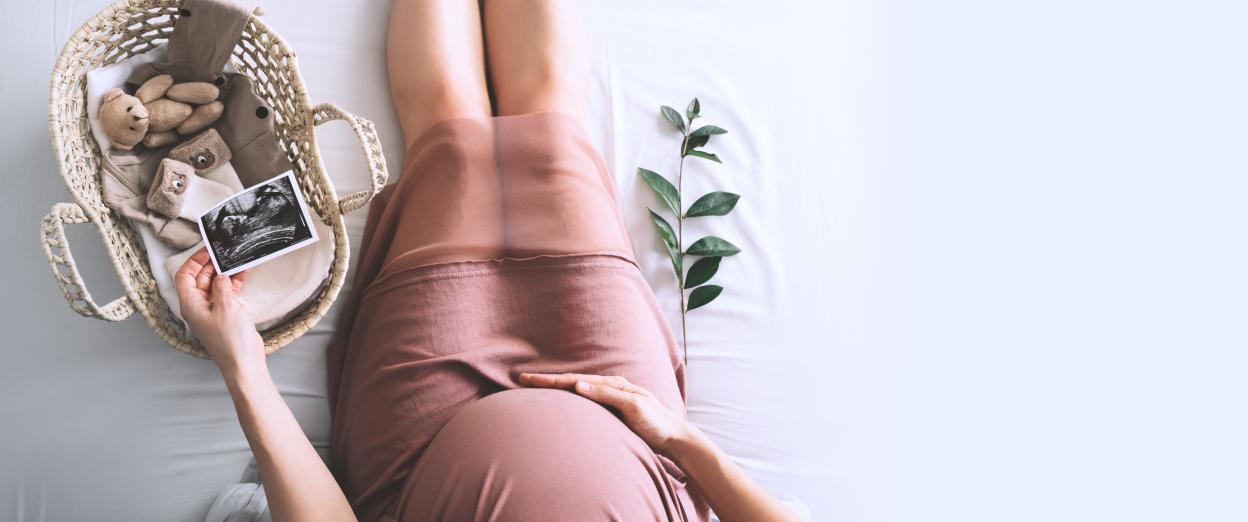 an expectant mother sitting on the floor holding her stomach, while looking at an ultrasound picture and new baby iteams