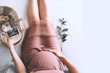 an expectant mother sitting on the floor holding her stomach, while looking at an ultrasound picture and new baby iteams