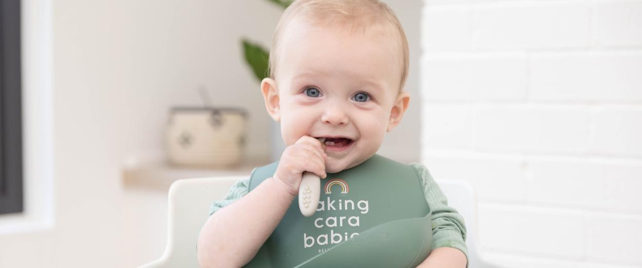 happy baby sitting in high chair with bib self feeding