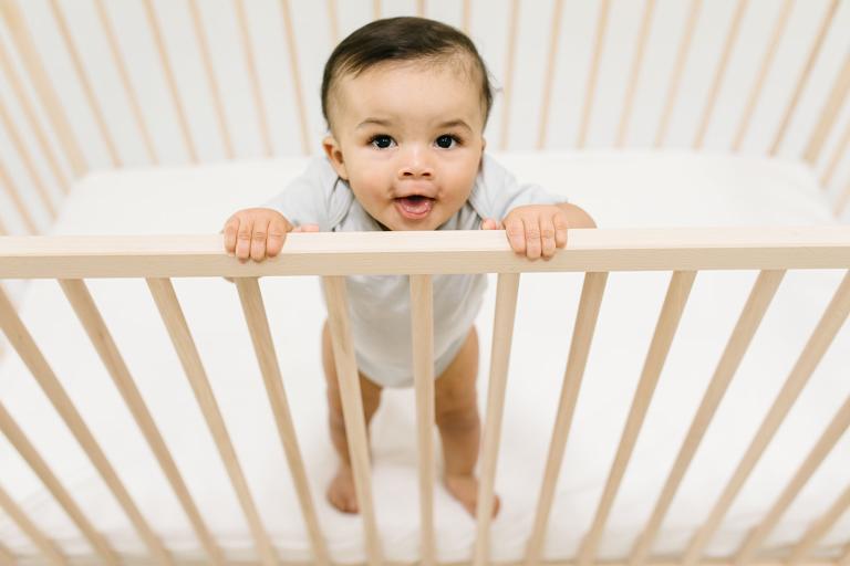 baby standing in crib with crib mattress lowered for safety