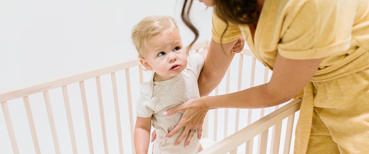 mom trying to put older baby with separation anxiety into crib with her lovey