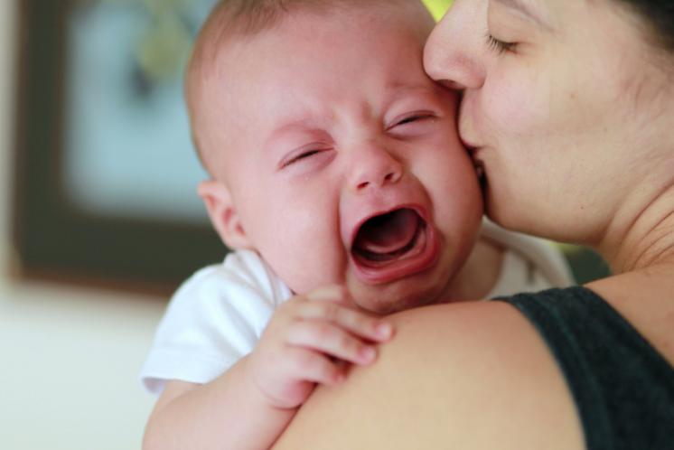 Baby fighting sleep and crying on mom's shoulder while she gives him a kiss
