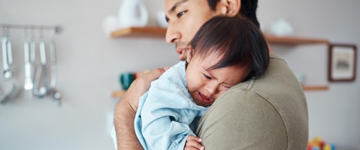 dad holding crying baby on his shoulder, trying to help him go to sleep