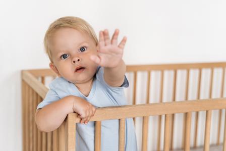 baby standing in crib reaching toward camera while refusing to nap