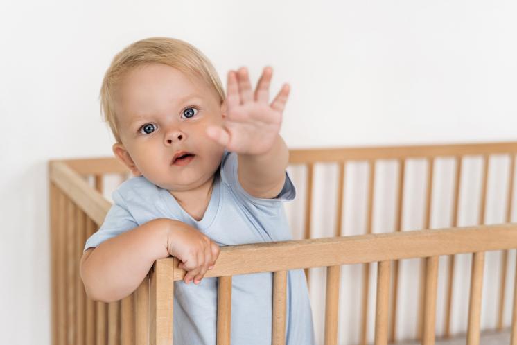 baby standing in crib reaching toward camera while refusing to nap