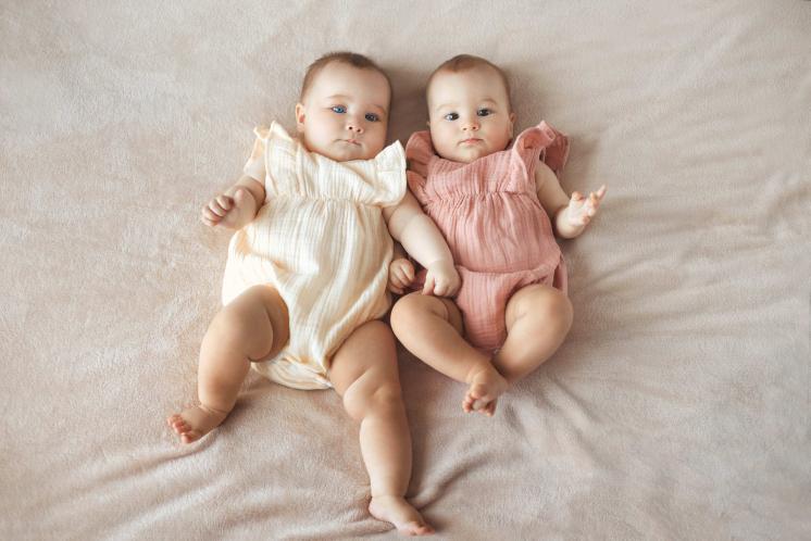 baby girl twins looking a the camera, one in off white the other in blush pink rompers
