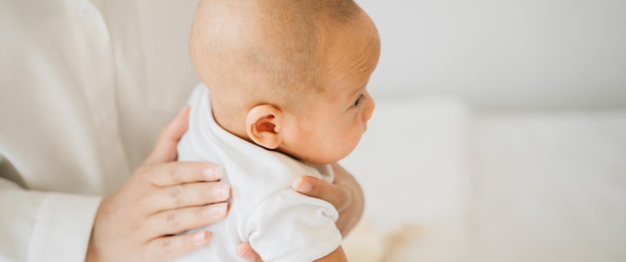 Light and bright white image of parent attempting to burp a young baby.