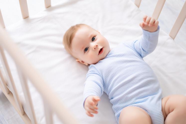 Baby boy wearing a blue striped onesie looking at that camera from inside his crib