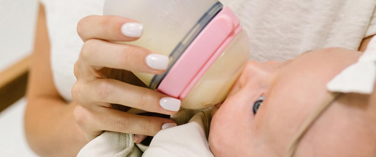 baby distracted while eating a bottle and being held by Mom