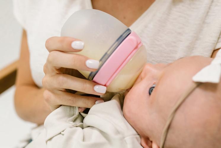 baby distracted while eating a bottle and being held by Mom