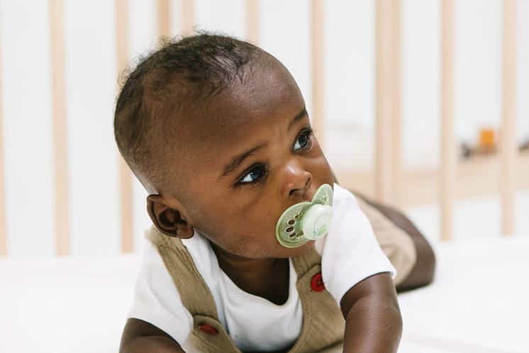 five month old on tummy in crib with pacifier looking around the room