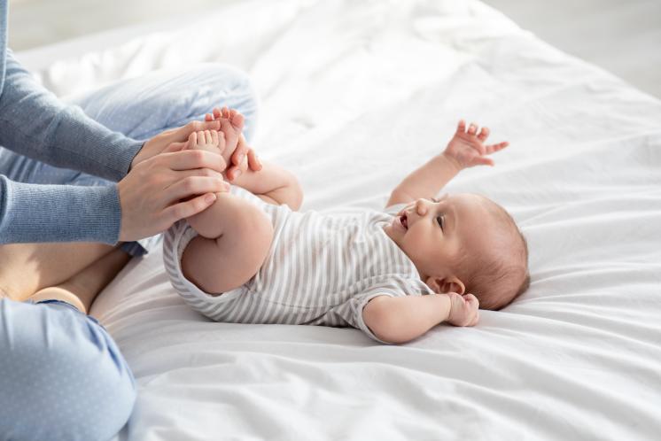 awake baby laying on white bed with parent doing exercises to relieve gas before bed