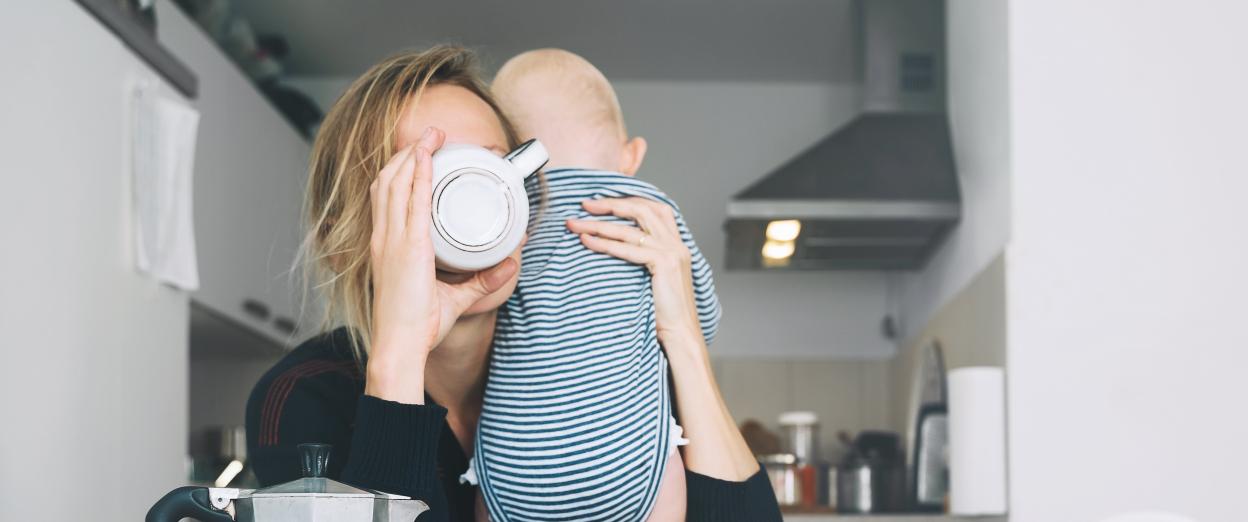Mom drinking out of coffee cup holding baby on her shoulder