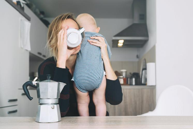 Mom drinking out of coffee cup holding baby on her shoulder