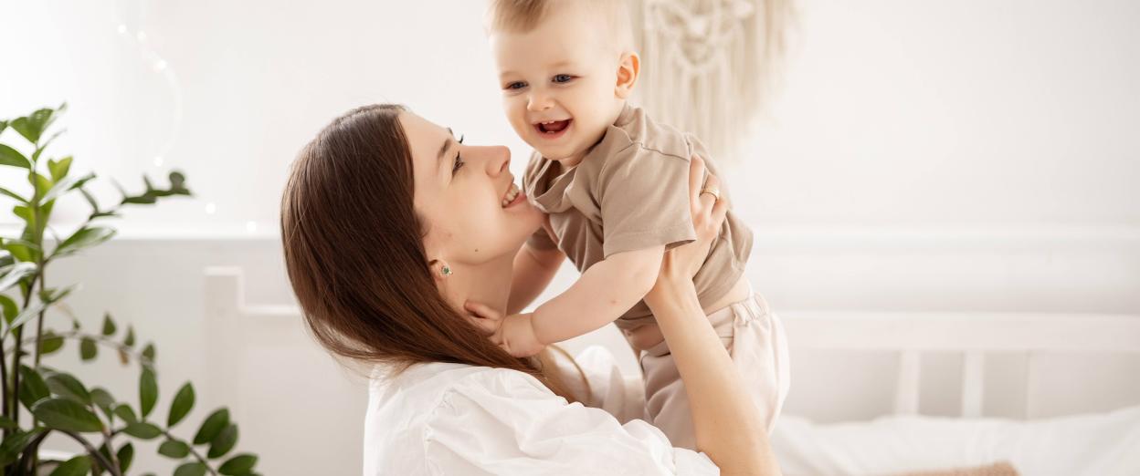 mom holding baby up above her and gazing at baby smiling