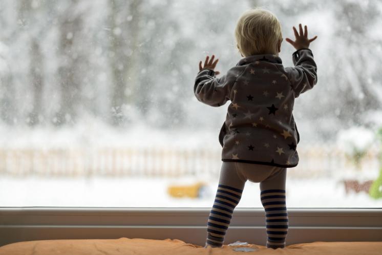 toddler dressed warmly looking out window at the snow