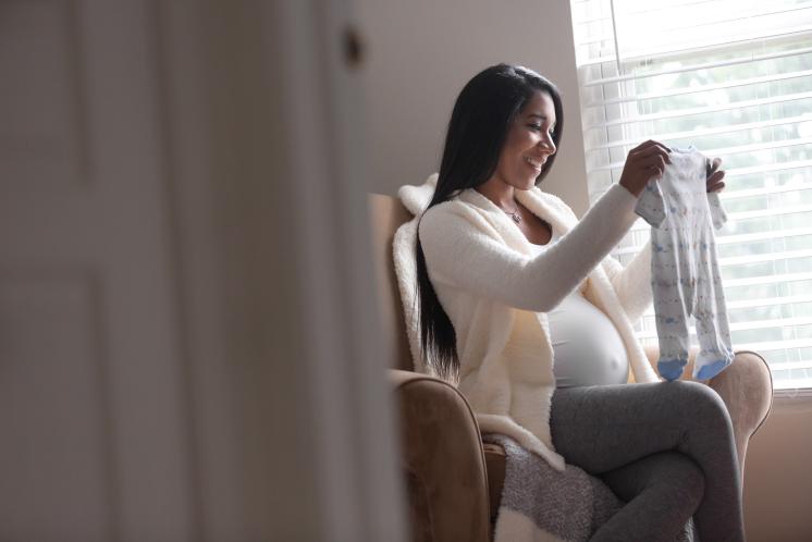 Pregnant mother happily going through newborn clothes in a rocking chair.