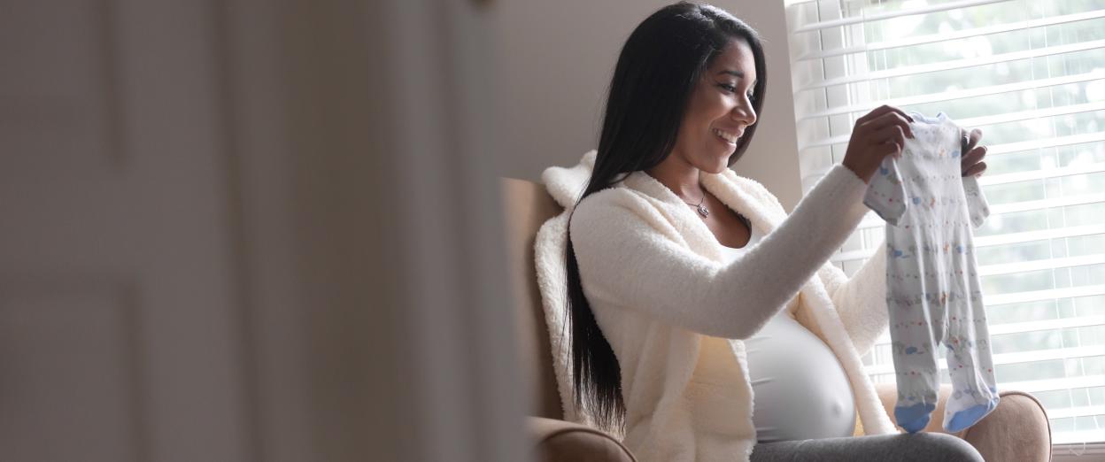 Pregnant mother happily going through newborn clothes in a rocking chair.