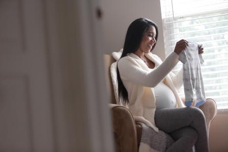 Pregnant mother happily going through newborn clothes in a rocking chair.