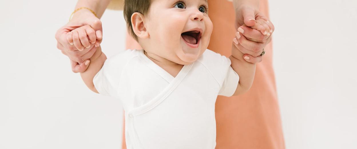 happy toddler working on learning to walk by holding mom's hands