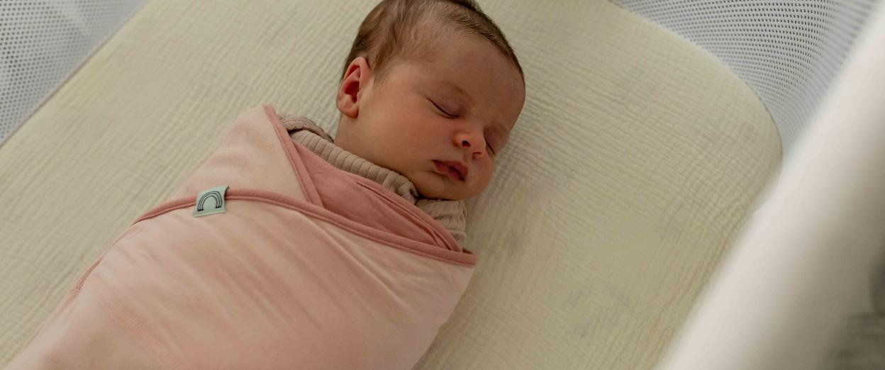 swaddled newborn asleep in crib