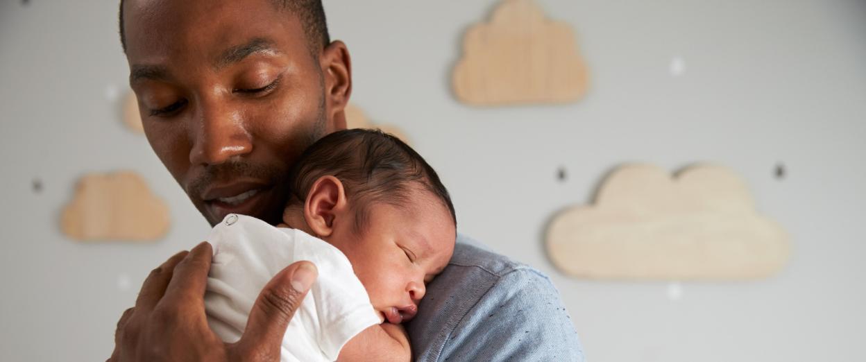 newborn baby sleeping on dad's shoulder in nursery with clouds on the wall