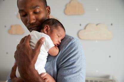 newborn baby sleeping on dad's shoulder in nursery with clouds on the wall