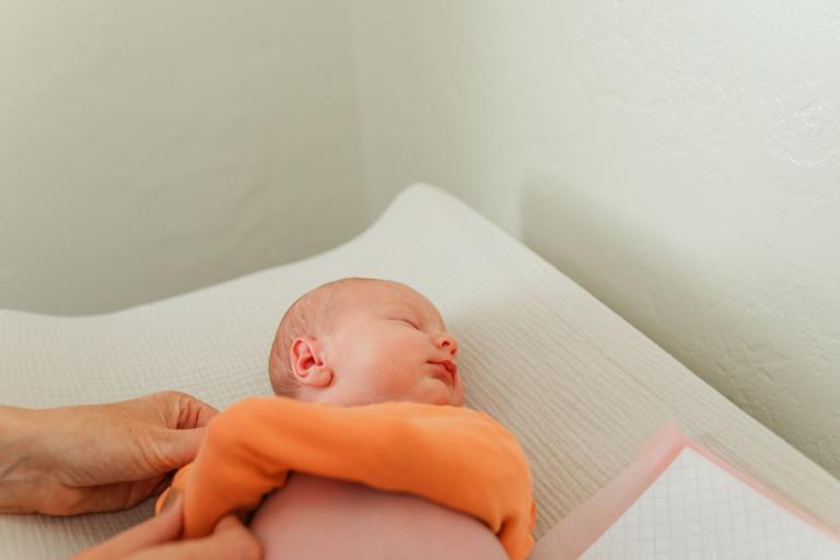 baby laying on changing table with onesie pulled up over his arms to contain them during diaper change