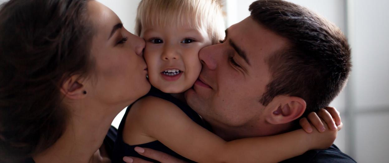 up close shot of a mom and dad kissing opposite cheeks of toddler
