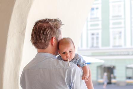 man facing away from camera with baby on his shoulder who is facing the camera as baby spits up over Dad's shoulder