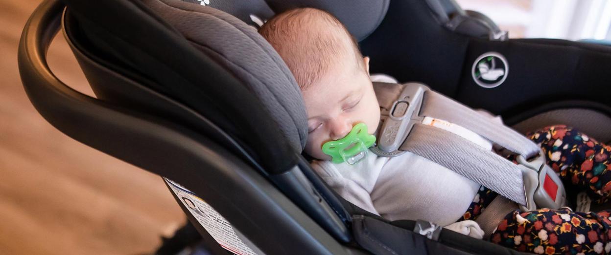 newborn baby safely sleeping in car seat with pacifier