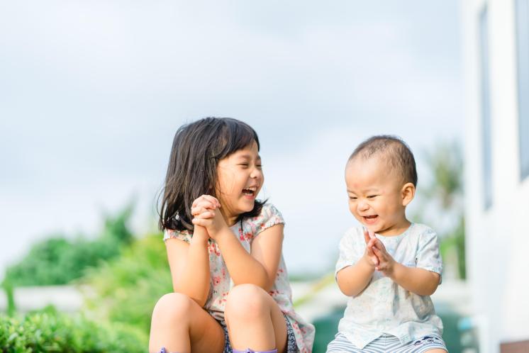 Baby brother laughing with big sister sitting on the porch after school