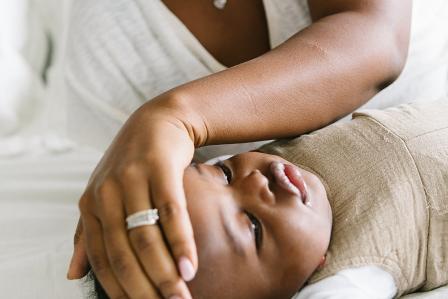 sick baby laying on bed looking away while mom feels his forehead for warmth