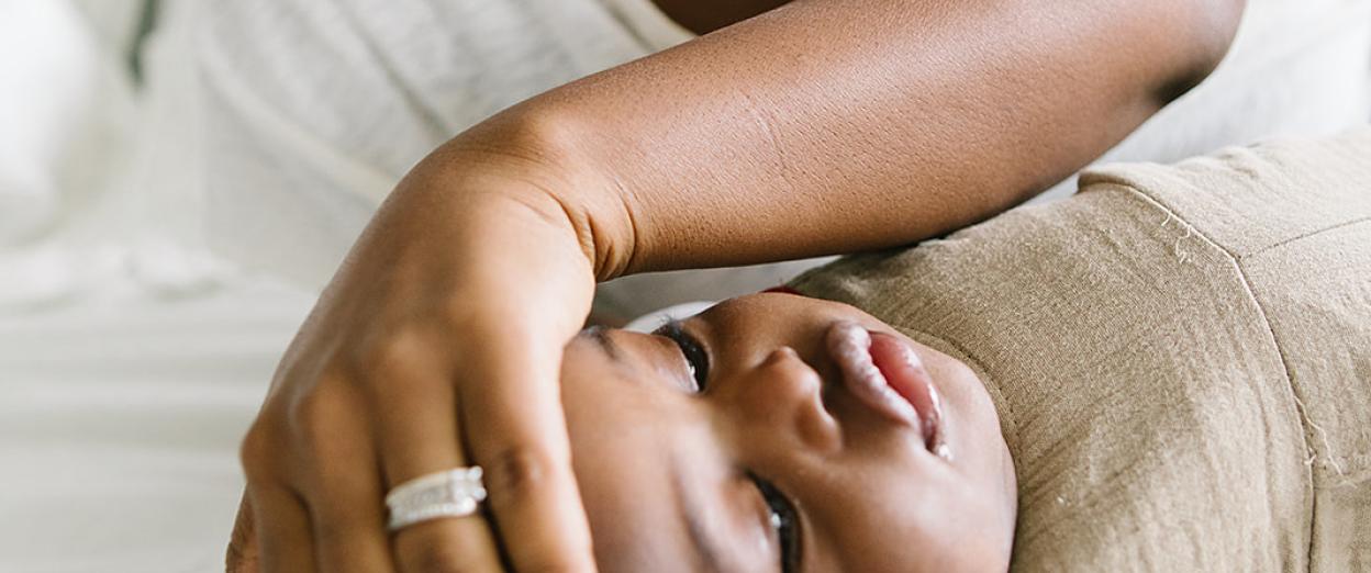 sick baby laying on bed looking away while mom feels his forehead for warmth