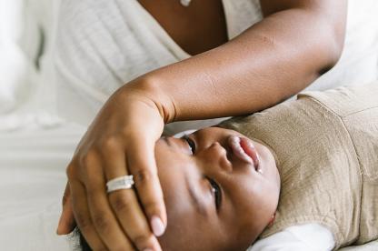sick baby laying on bed looking away while mom feels his forehead for warmth