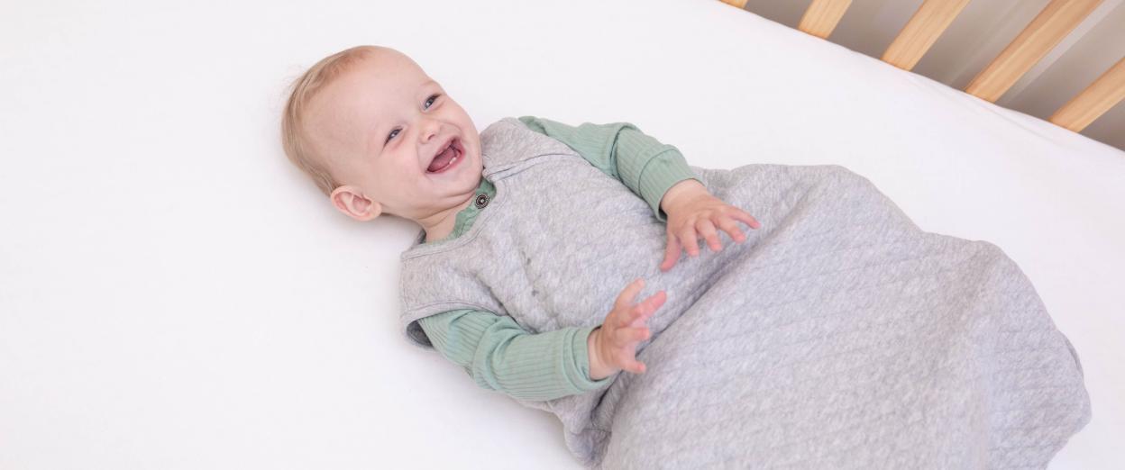 baby in crib smiling wearing a sleep sack