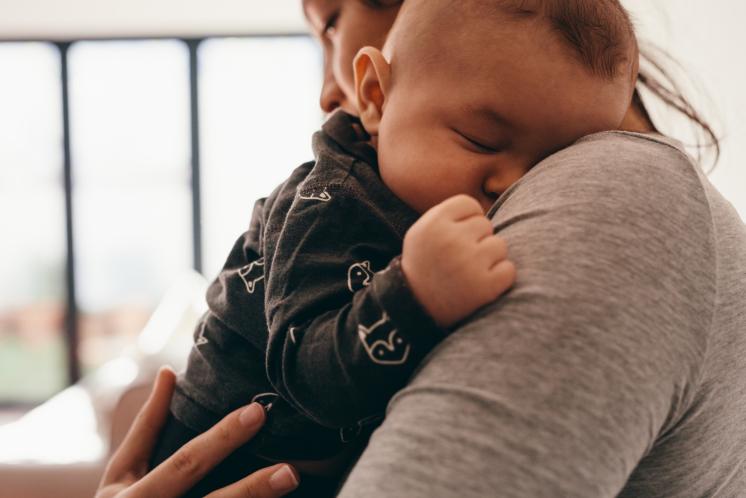 Sleeping baby being held by mom, up on shoulder, in a well lit room