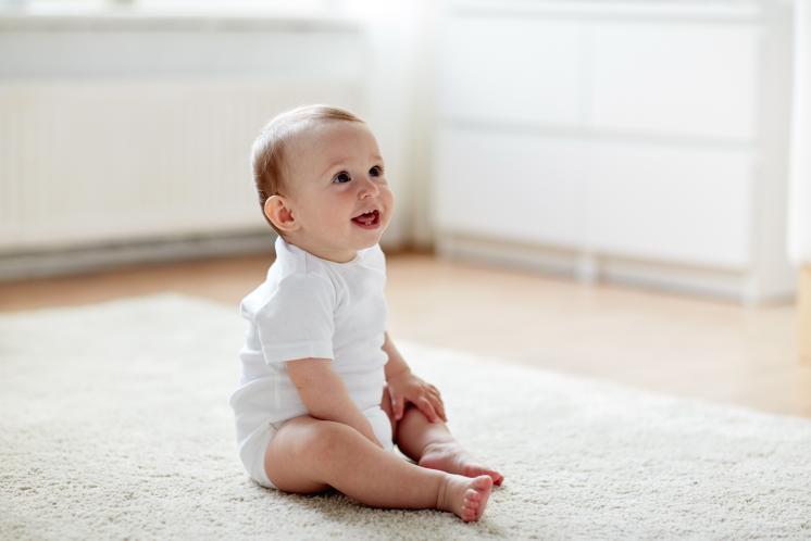 Baby wearing white onesie baby sitting up happily.