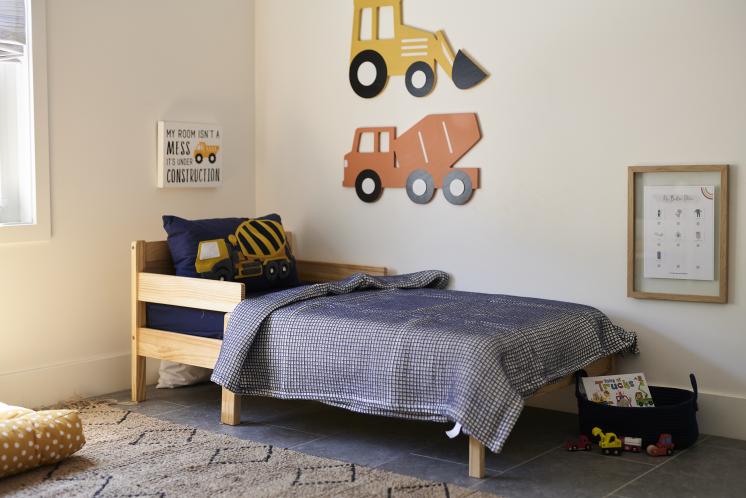 toddler bed with navy blue bedding and construction vehicle decorations around the room