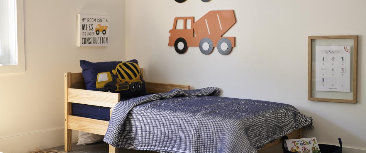 toddler bed with navy blue bedding and construction vehicle decorations around the room
