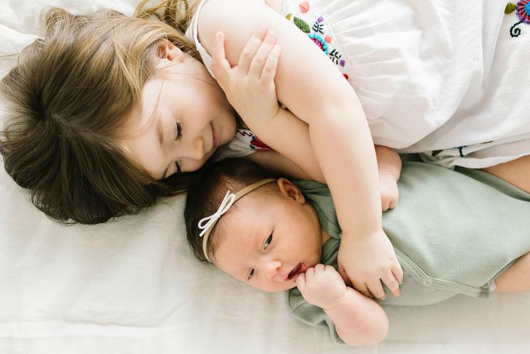 toddler girl smiling while laying with newborn sister
