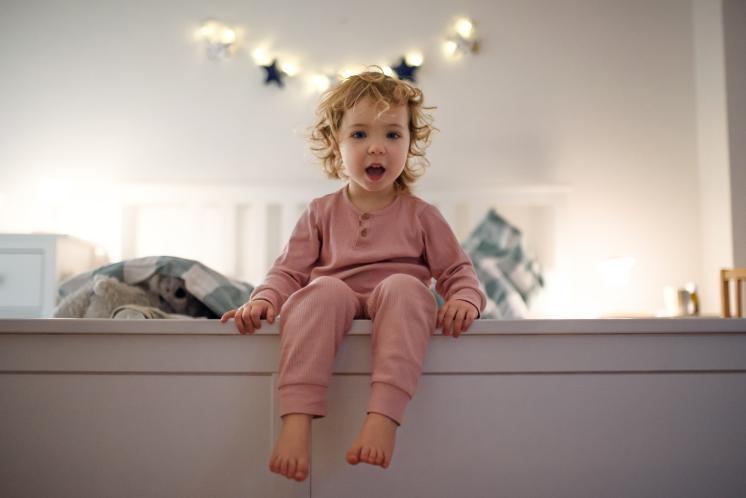 Toddler sitting on the edge of bed about to get out