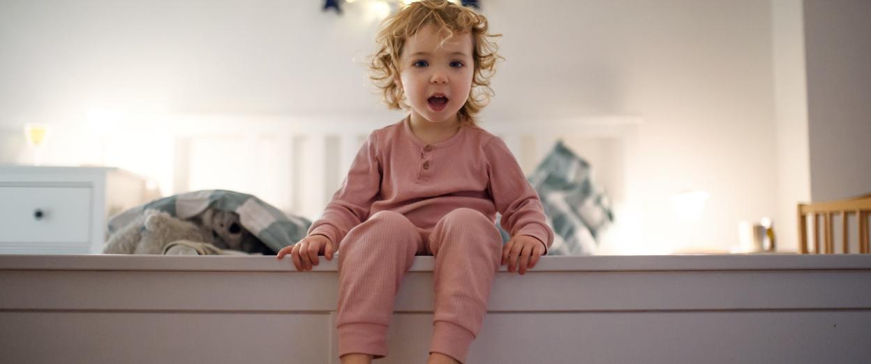 Toddler sitting on the edge of bed about to get out
